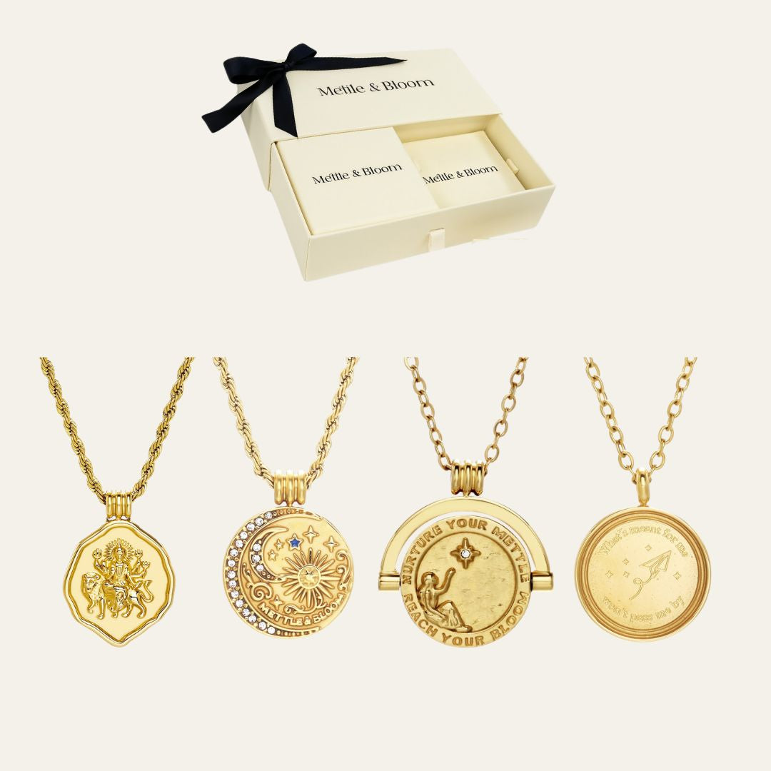 Four gold-toned pendant necklaces displayed below an open cream-colored Meltie & Bloom gift box with a black ribbon, on a light beige background.