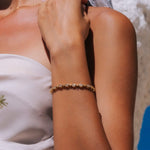 A delicate gold bracelet with small clear stones worn on a woman's wrist, shown in a close-up lifestyle shot.
