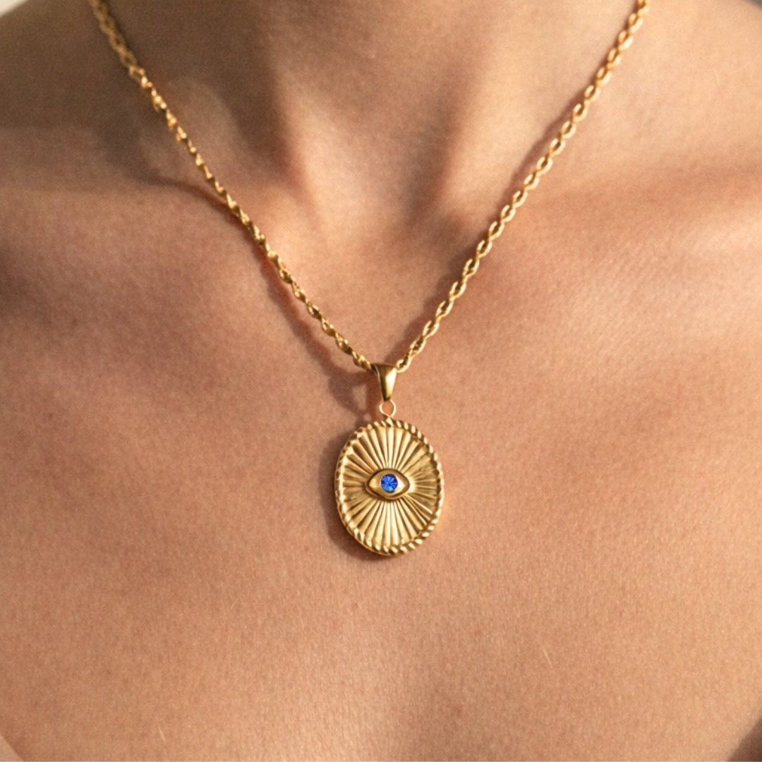 Oval shaped gold with a vibrant blue center stone. A modern talisman designed to protect your peace and elevate your everyday. Featuring radiant sunburst detailing and a striking blue centre stone, this piece is your subtle statement. bold in meaning, timeless in style.