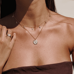 Gold to the moon and back necklace layered with the white chakra necklace on a person's neck. these two necklaces are perfect for layering or wearing solo.