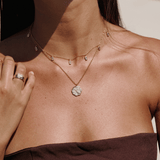 Gold to the moon and back necklace layered with the white chakra necklace on a person's neck. these two necklaces are perfect for layering or wearing solo.