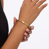 Gold bangle with zirconia stones and a bamboo inspired design wornn on a wrist with a plain background