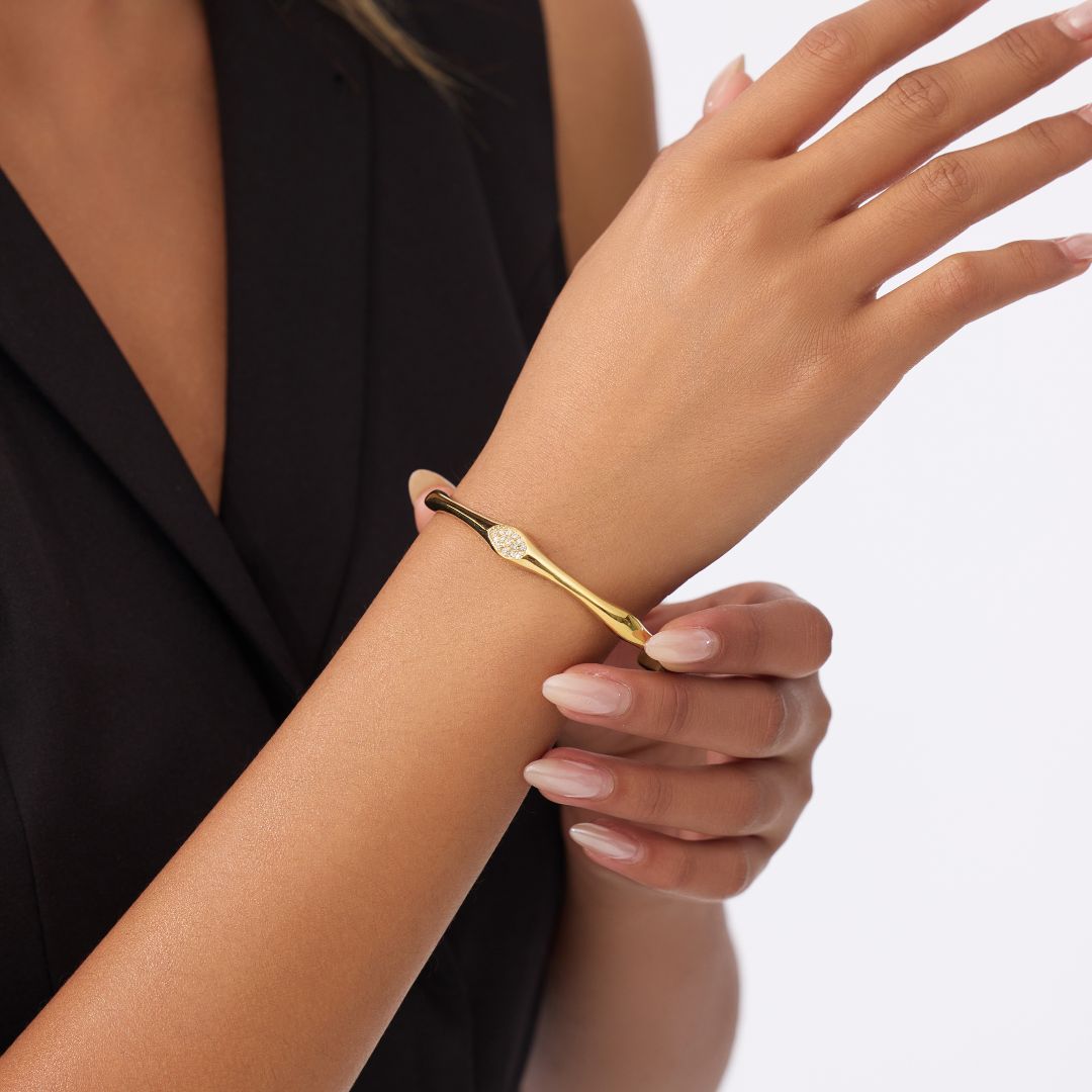 Gold bangle with zirconia stones and a bamboo inspired design wornn on a wrist with a plain background