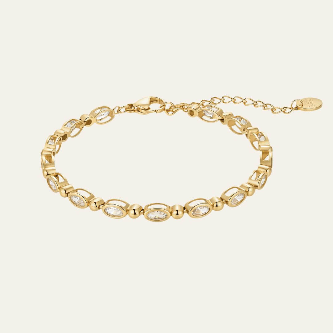 A gold chain bracelet featuring alternating oval bezel-set clear stones and polished gold links, displayed on a light cream background.