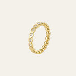 A gold beaded ring with a row of small clear gemstones set along the front, shown on a light cream background.