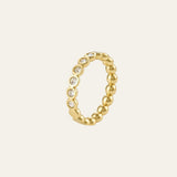A gold beaded ring with a row of small clear gemstones set along the front, shown on a light cream background.
