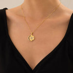 Gold necklace with a pendant on a person wearing a black top.