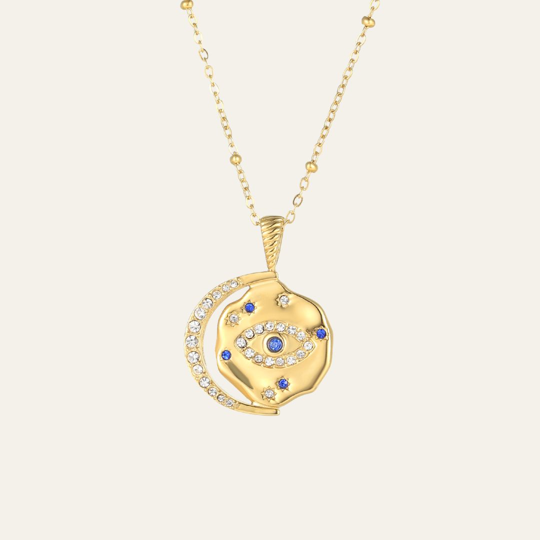 Gold necklace with an eye-shaped pendant on a beige background. This is Mettle & Bloom's signature style.
