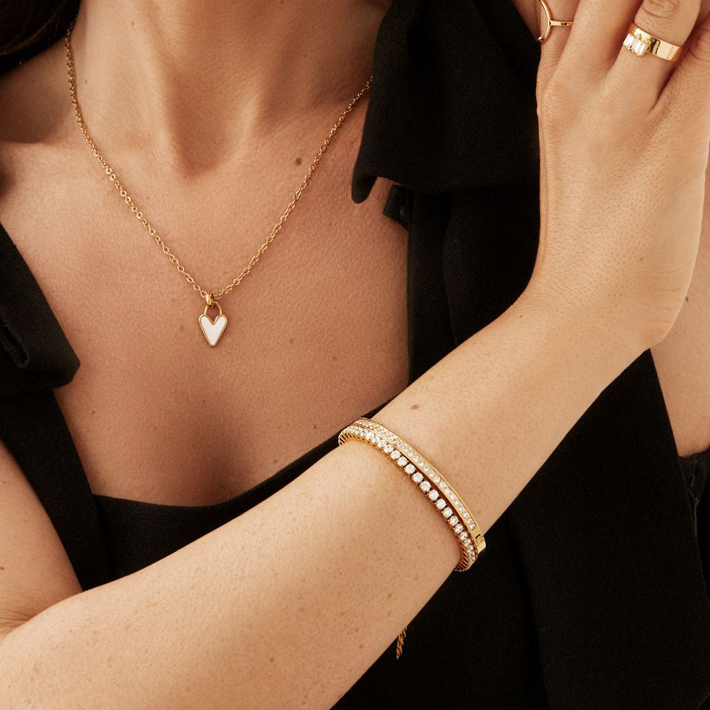 Close-up of a person wearing gold jewelry including a necklace, bracelet, and rings. the focus is on the heart necklace