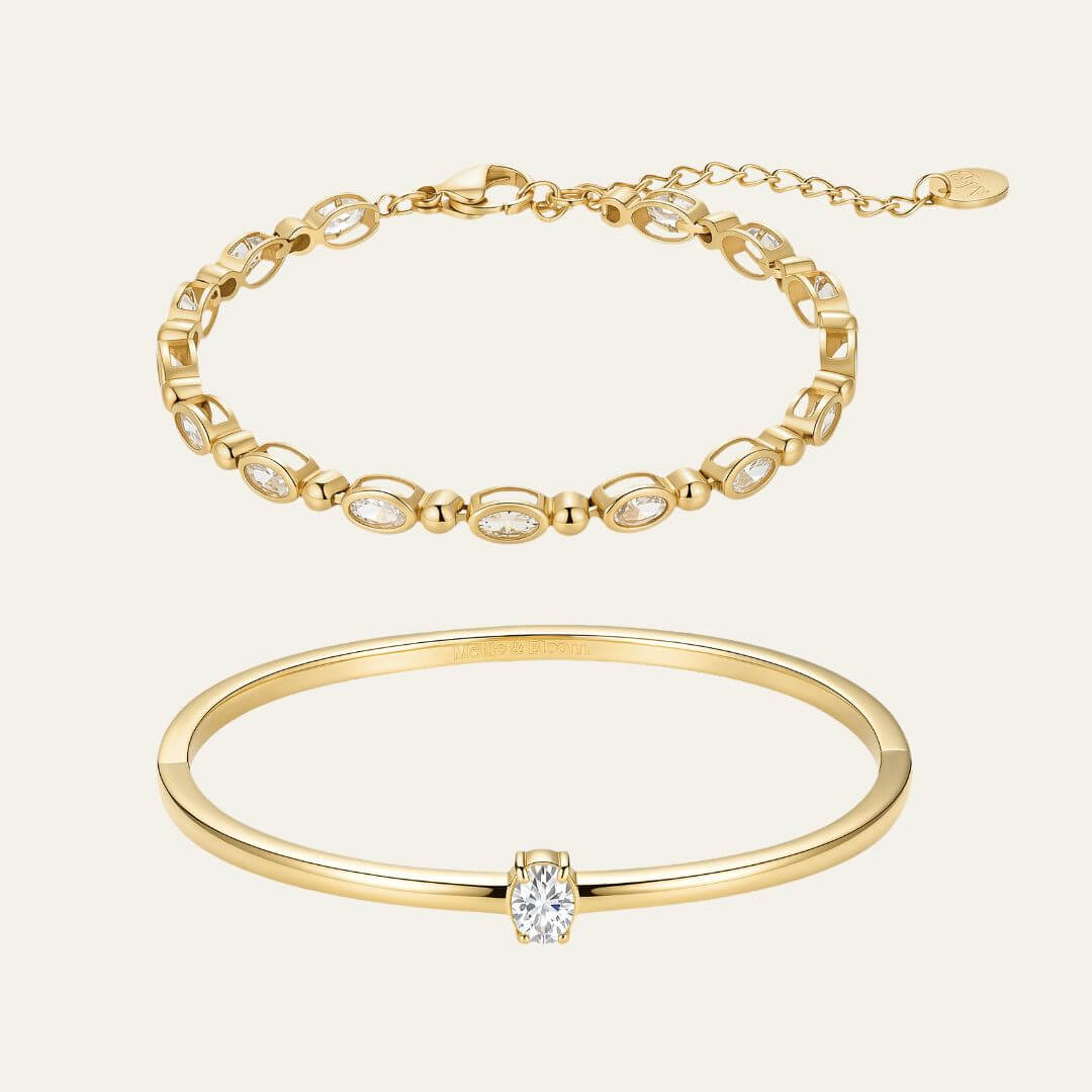 Two gold bracelets on a light warm grey background: a tennis bracelet with repeating oval clear stones and a slim bangle bracelet with a single clear stone at the center.