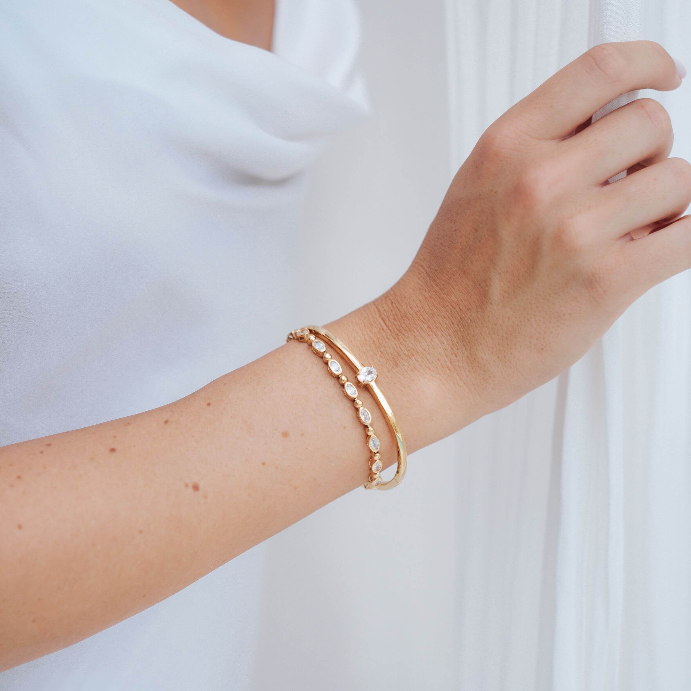 the person has two bracelets on her wrist. She stacked the Ritz Bangle and the Bezel & Bead Tennis Bracelet, both designed by Mettle & Bloom