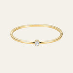 A delicate yellow gold bangle bracelet with a single rectangular-cut clear gemstone in a prong setting, shown against a solid off-white background.