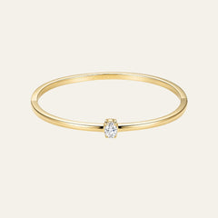 A delicate yellow gold bangle bracelet with a single rectangular-cut clear gemstone in a prong setting, shown against a solid off-white background.