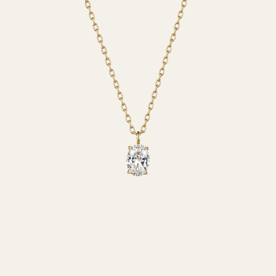 A delicate gold chain necklace with a single oval-cut clear gemstone pendant in a prong setting, shown against a solid off-white background.