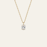 A delicate gold chain necklace with a single oval-cut clear gemstone pendant in a prong setting, shown against a solid off-white background.