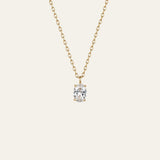 A delicate gold chain necklace with a single oval-cut clear gemstone pendant in a prong setting, shown against a solid off-white background.