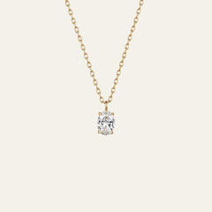 A delicate gold chain necklace with a single oval-cut clear gemstone pendant in a prong setting, shown against a solid off-white background.