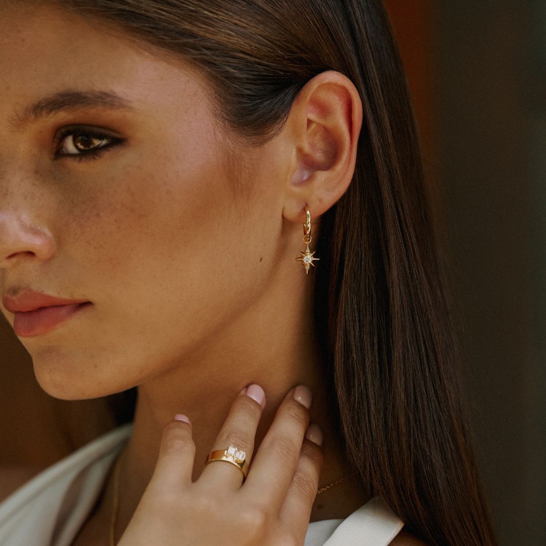 woman wearing the star drop earrings from mettle and bloom. they were designed in house by mettle and bloom. they are a hoop earring with a star suspended from it. 