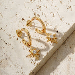 star drop earrings on a tile surface. They were designed in house by mettle and bloom. they are a hoop earring with a star suspended from it. 