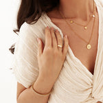 Woman wearing gold jewelry including a necklace, ring, and bracelet on a white background