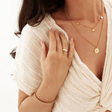 Woman wearing gold jewelry including a necklace, ring, and bracelet on a white background